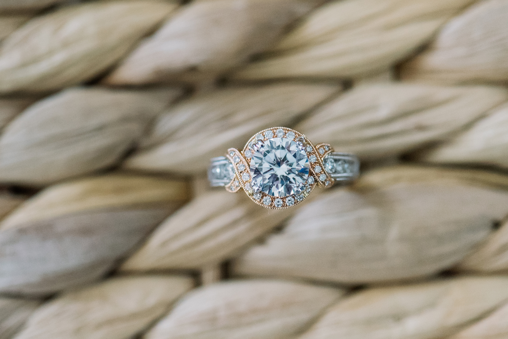 Two toned gold engagement ring with large round halo center on a woven grass background