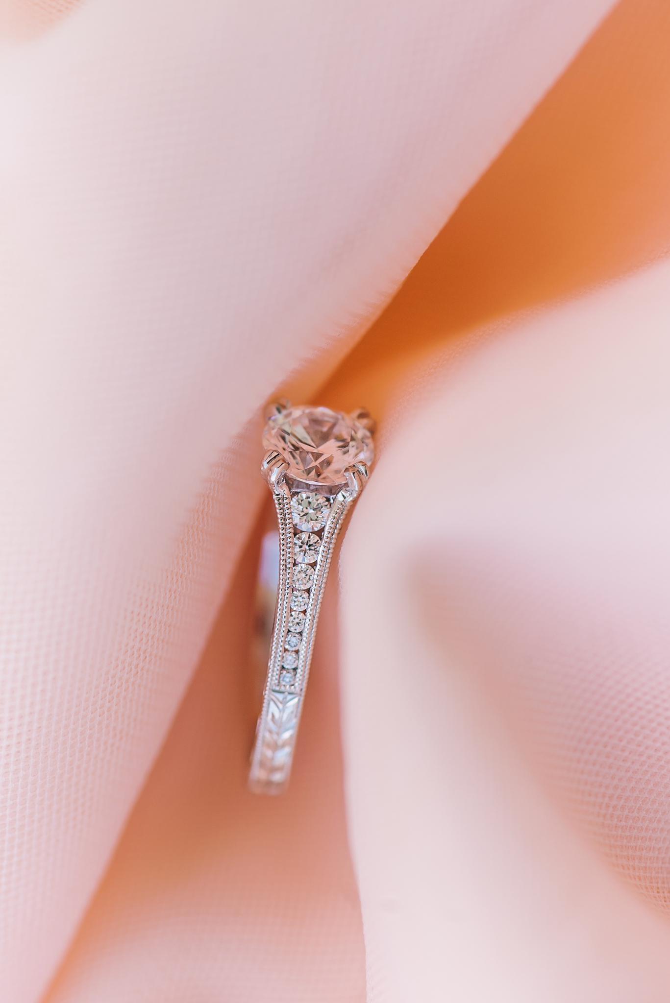 White gold and diamond engagement ring on a soft pink fabric background
