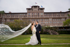 Bride and Groom on a field of grass with a grand old brick building in the background 