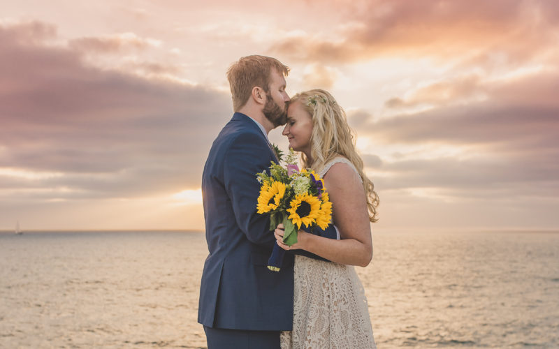 Couple kissing during wedding photoshoot during sunset with sunflowers and Kirk Kara rings