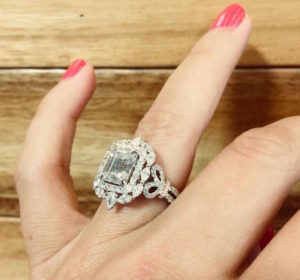 Large custom white gold and diamond engagement ring on hand with wood background.